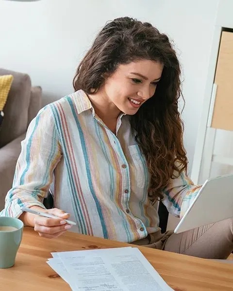 A physician, a Hispanic woman at her kitchen table with coffee reviewing her CV on a tablet, smiling.